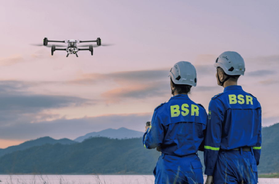 Two individuals in blue uniforms observing an Autel Alpha drone in the sky.