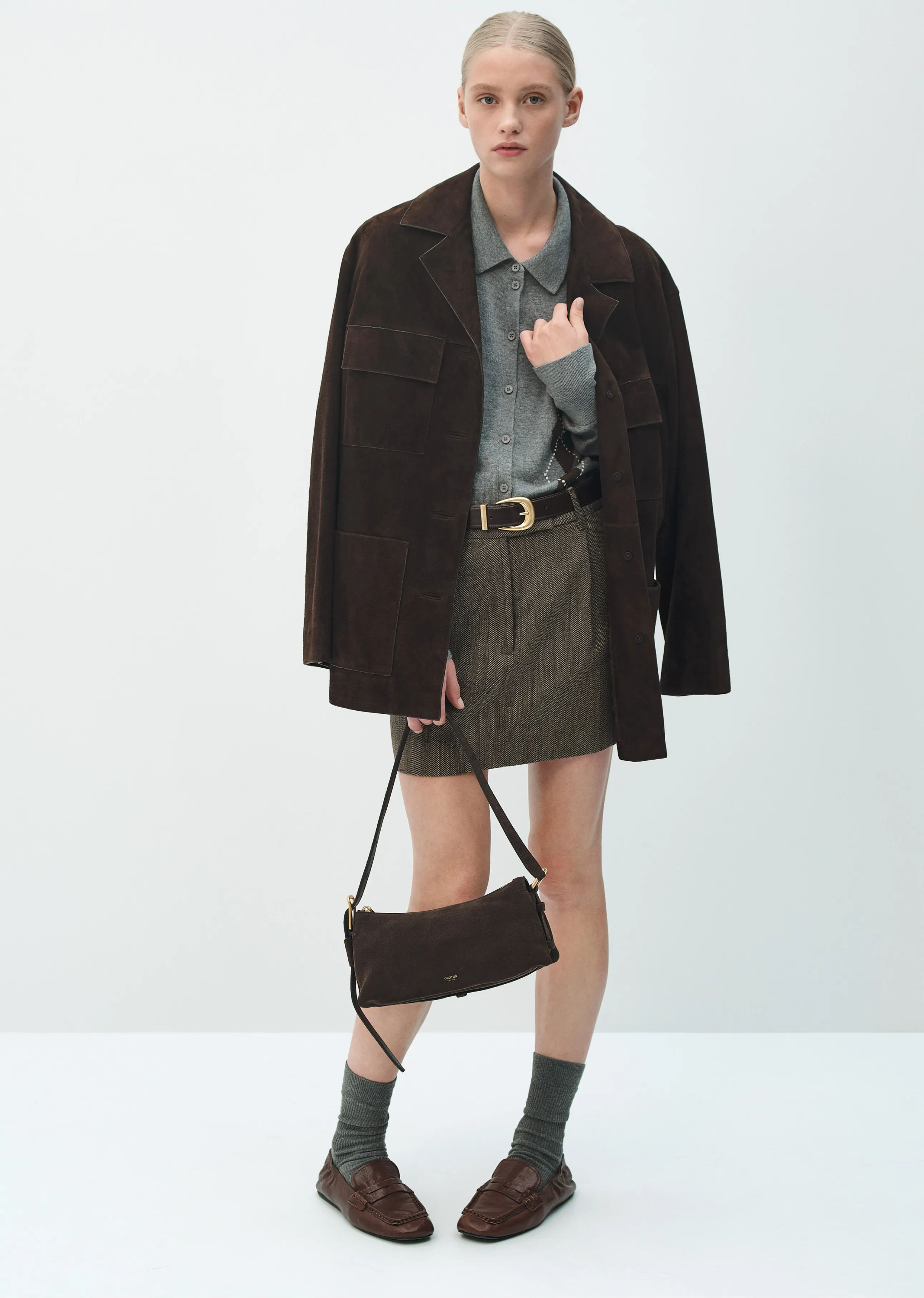 A person wearing a brown jacket, gray shirt, and skirt with a handbag.