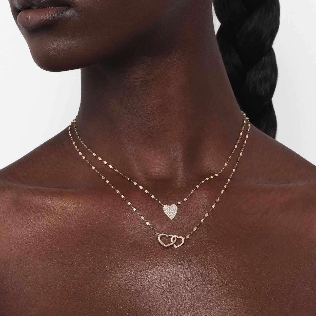 Close-up of a person wearing layered gold necklaces with heart designs.
