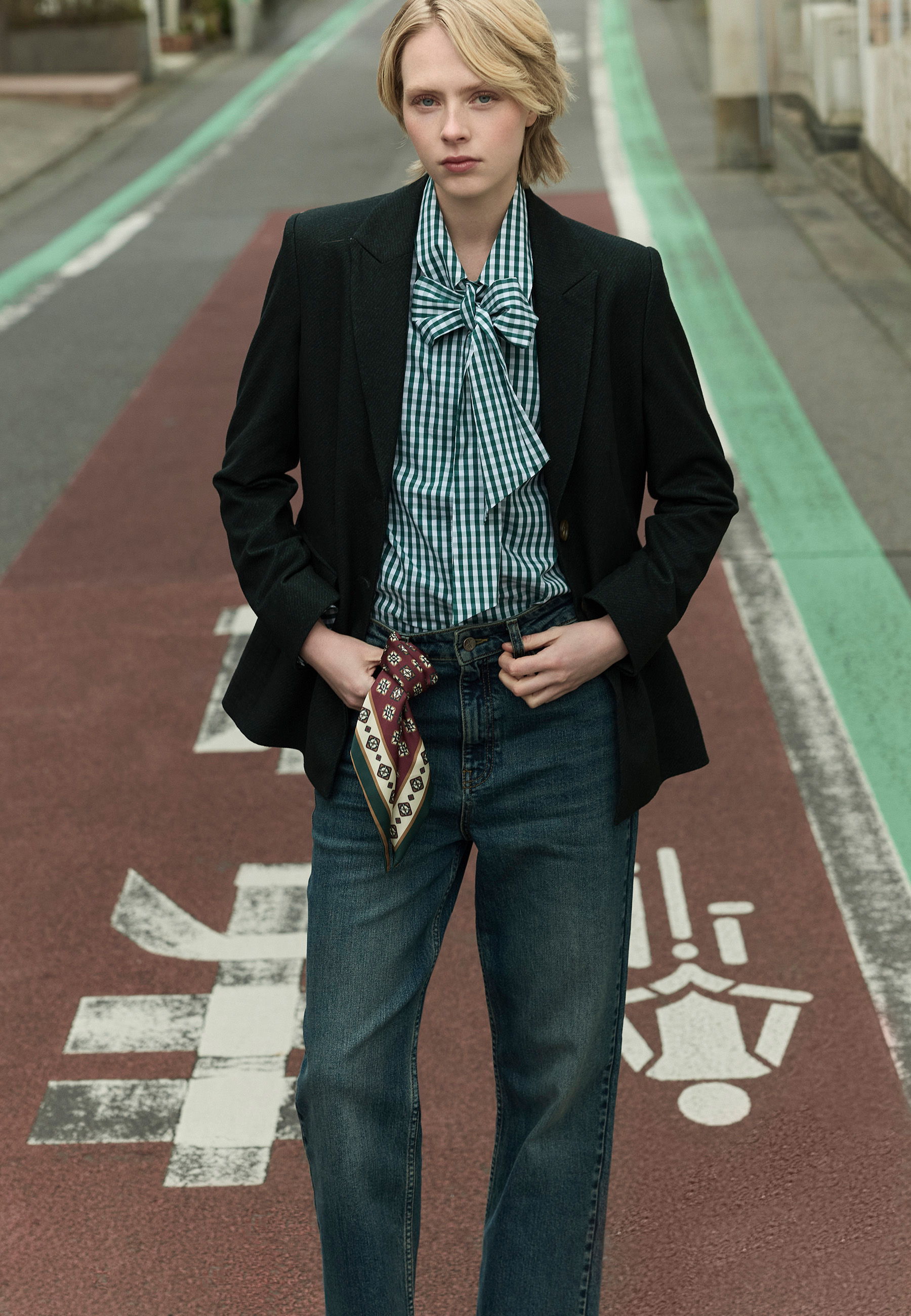 Person in a stylish outfit standing on a sidewalk with a green bike lane.