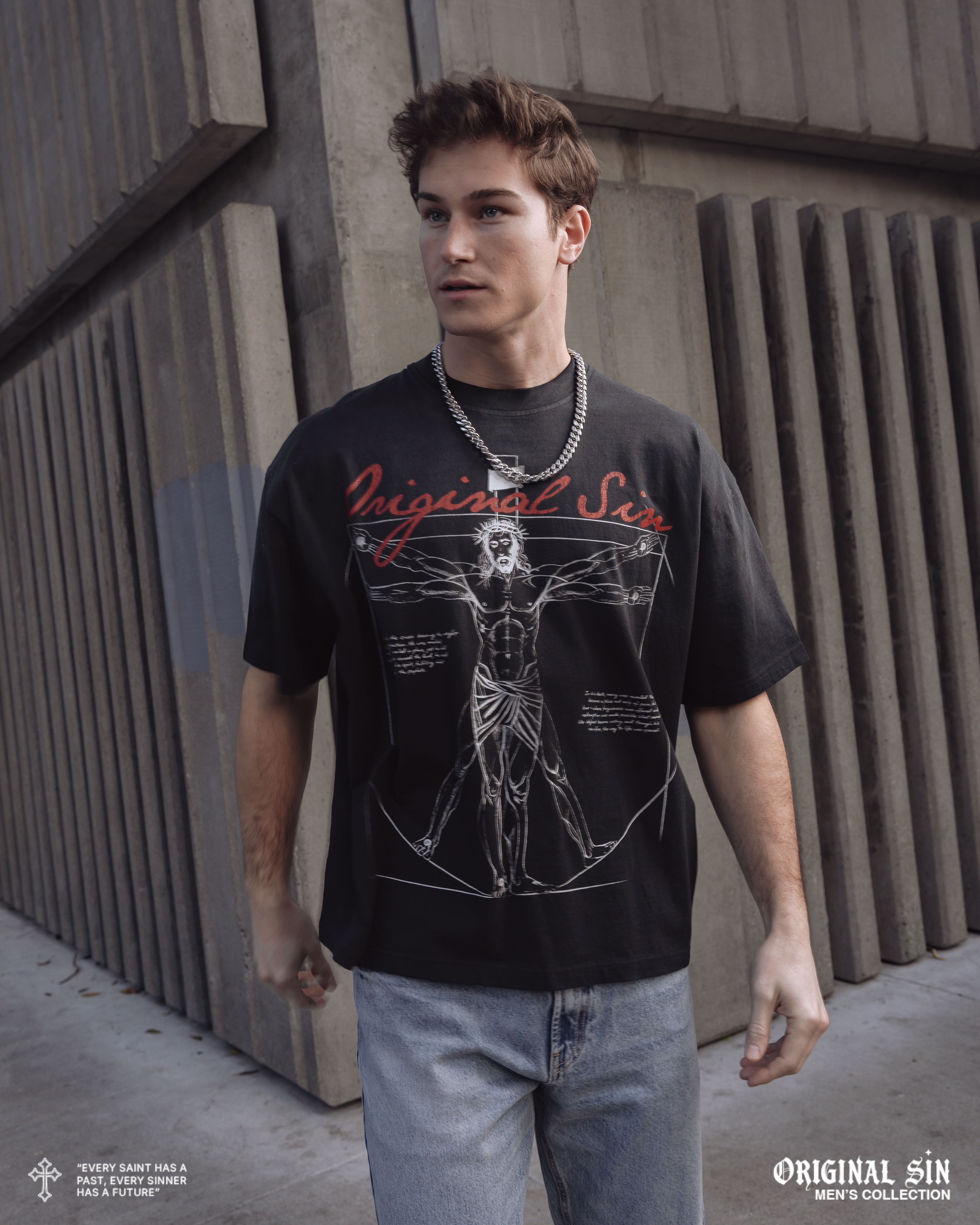 A young man wearing a graphic t-shirt and jeans stands outdoors.