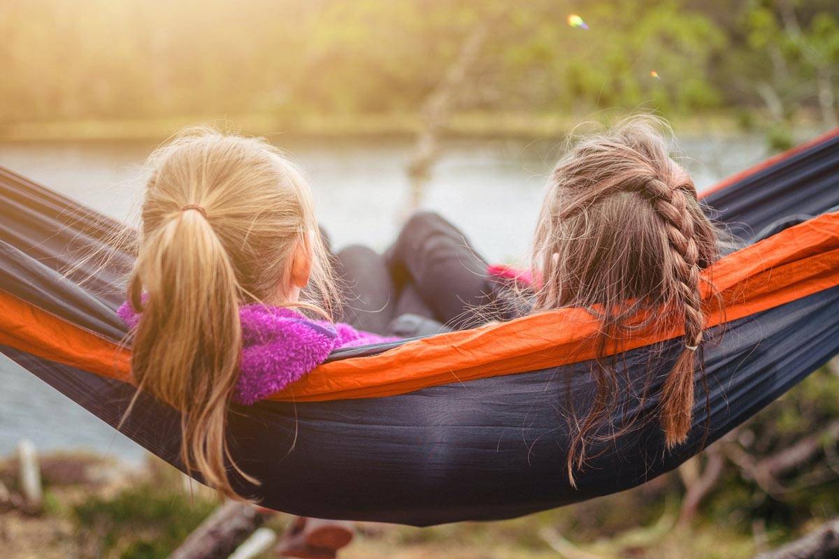 Two older girls relaxing in a hammock overlooking a lake