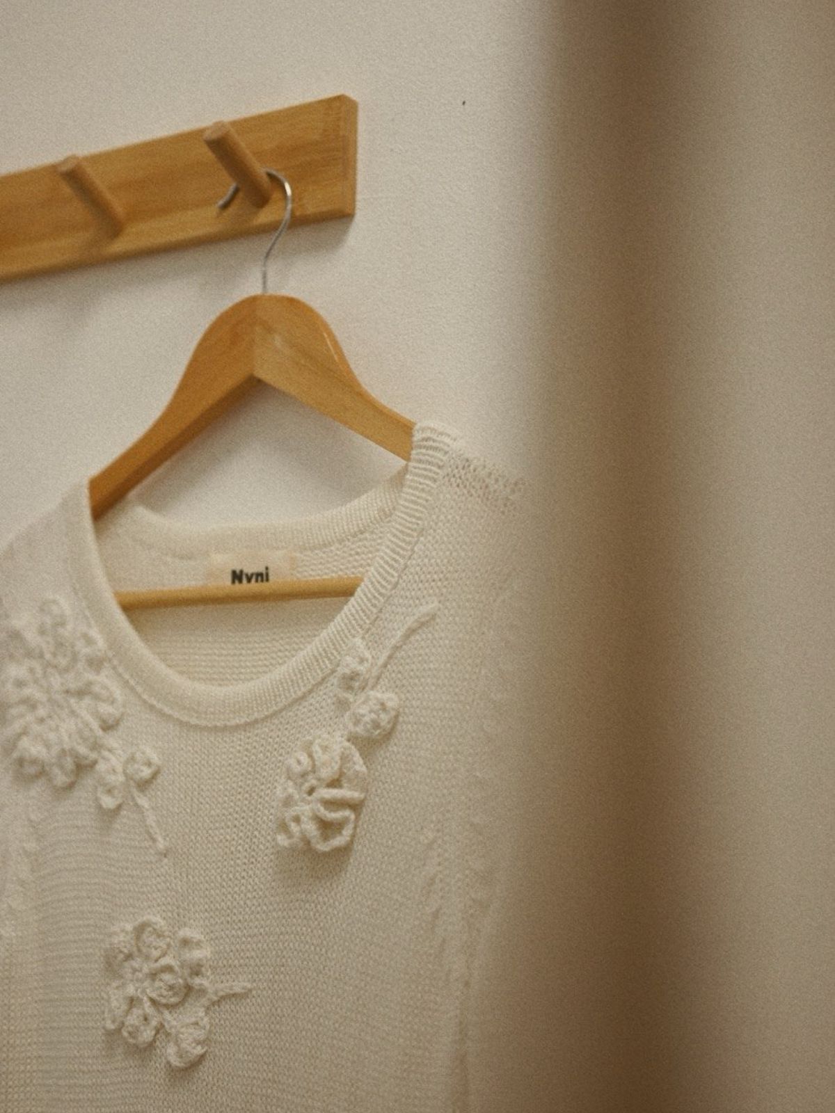 A white sweater with floral embellishments hanging on a wooden hanger.