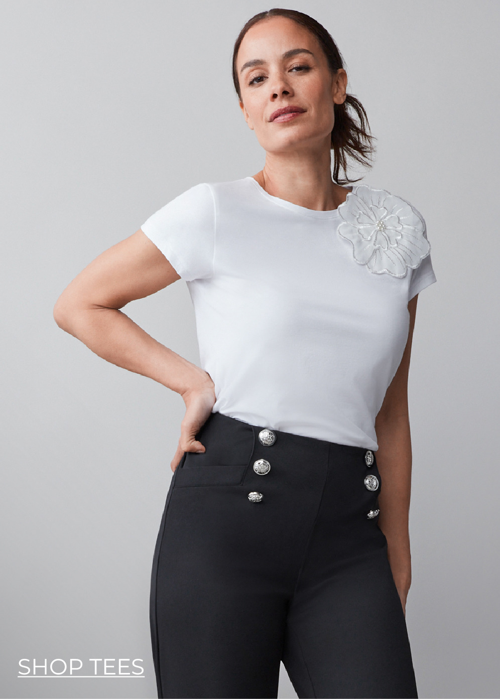 Model wearing a white shirt with a flower detail and high-waisted black pants.