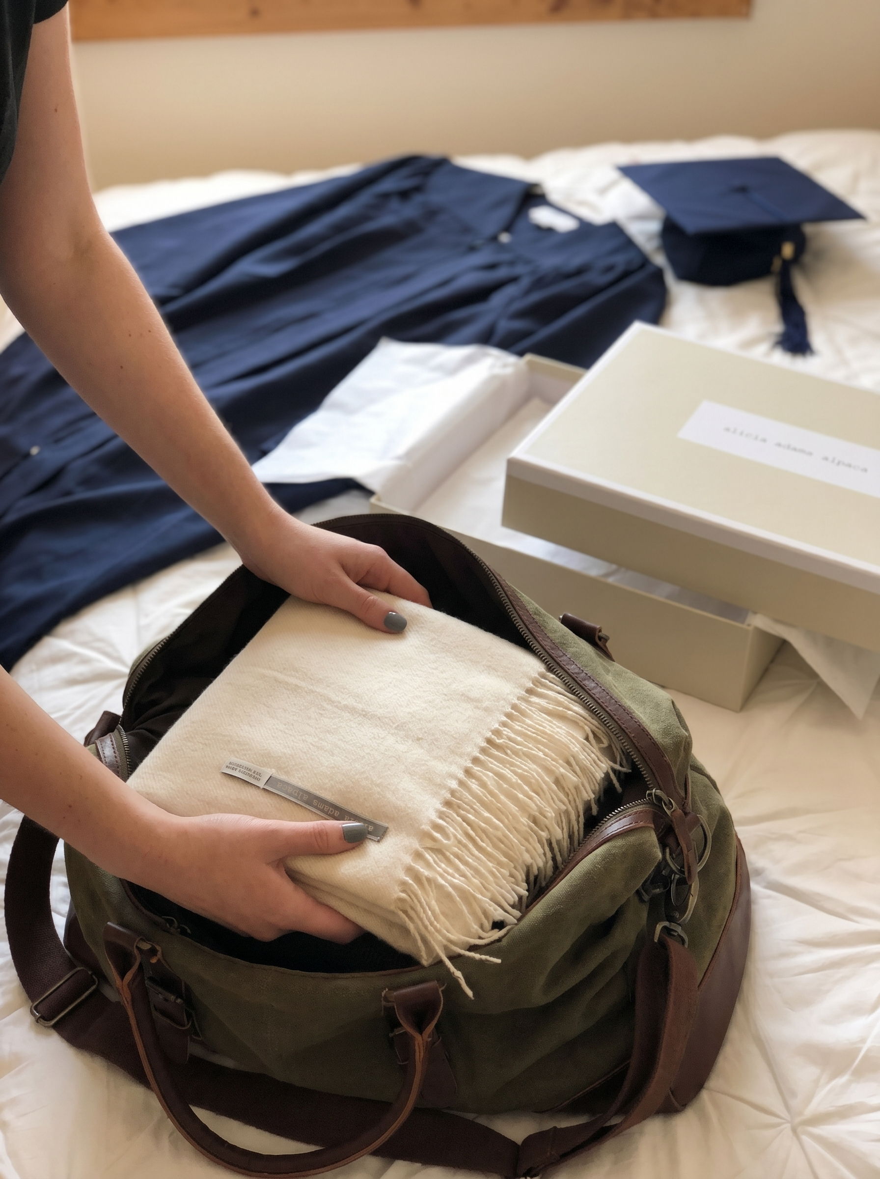 Person packing a bag with a blanket, graduation cap, and clothing.