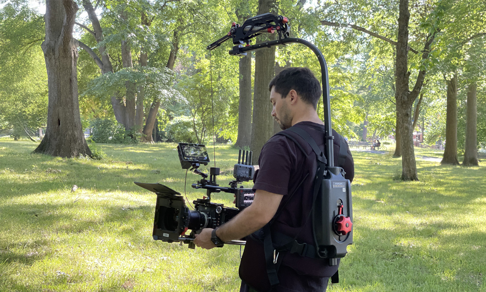 Person filming in a park with a camera on a stabilizer rig.