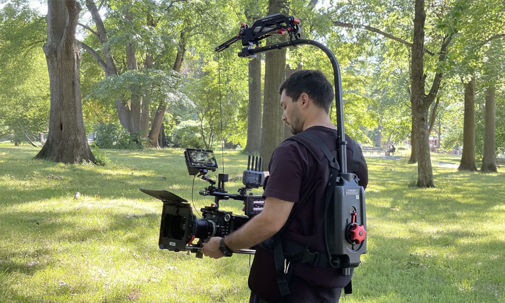 Person filming in a park with a camera on a stabilizer rig.
