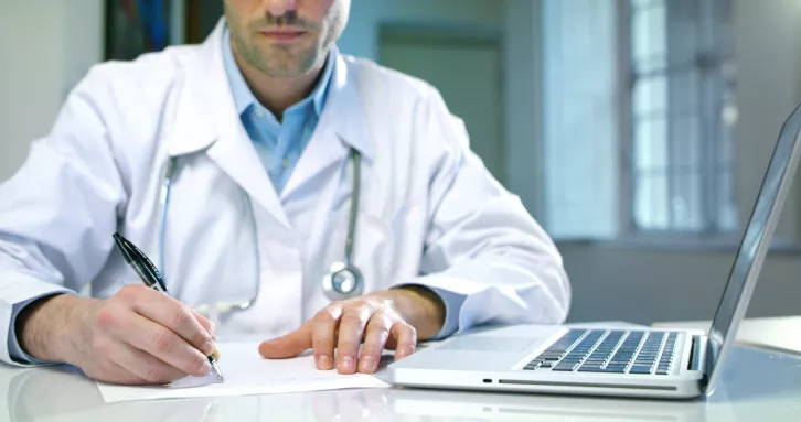Een dokter met laptop maakt apatientingen op papier