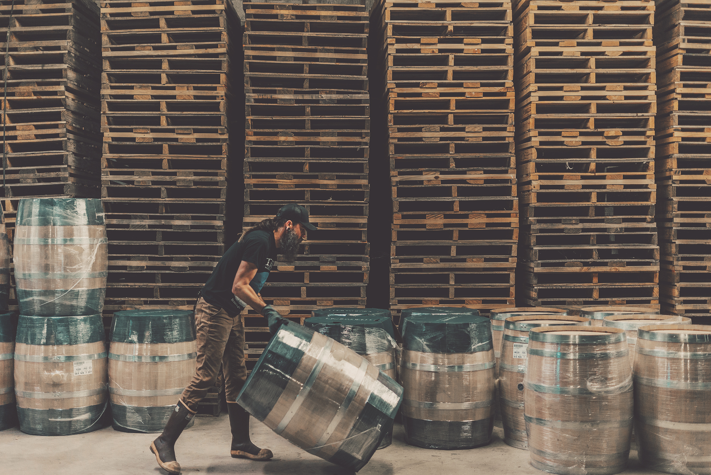 Person handling barrels in a warehouse with wooden pallets in the background.
