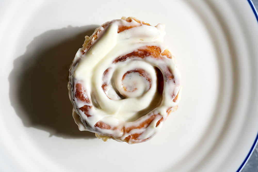 Fig and cinnamon bun topped with cream cheese icing on a white plate.