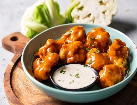 Bowl of buffalo cauliflower bites with ranch dressing and lettuce on the side.