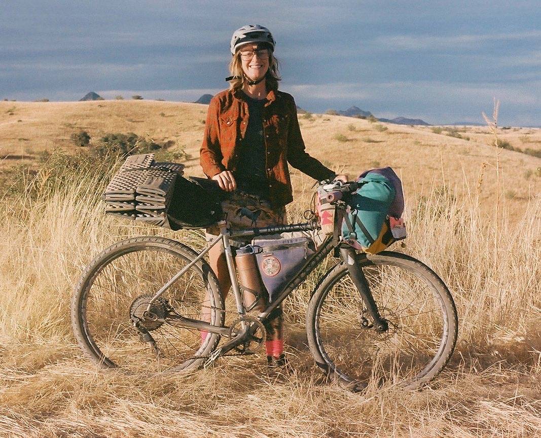 A woman stands with her fully-loaded Otso bikepacking rig on a prairie ridge in the Sonoran Desert of Arizona.