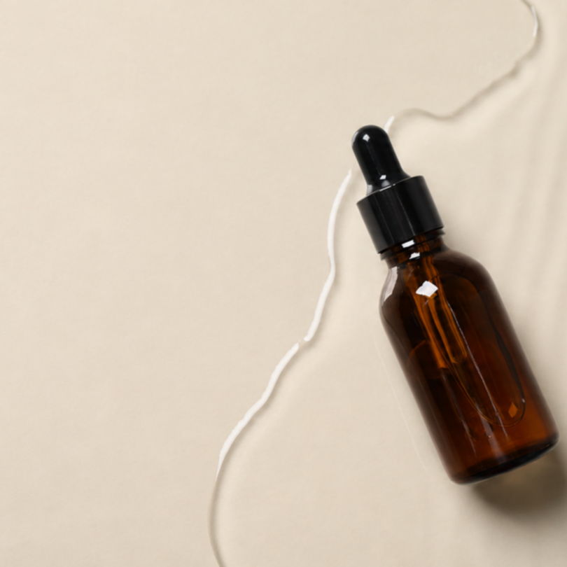 A brown glass dropper bottle on a light textured surface.