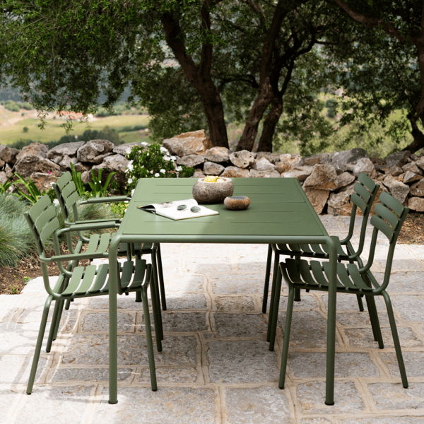 Powder-coated aluminum outdoor dining table and chairs on a stone patio beneath mature trees