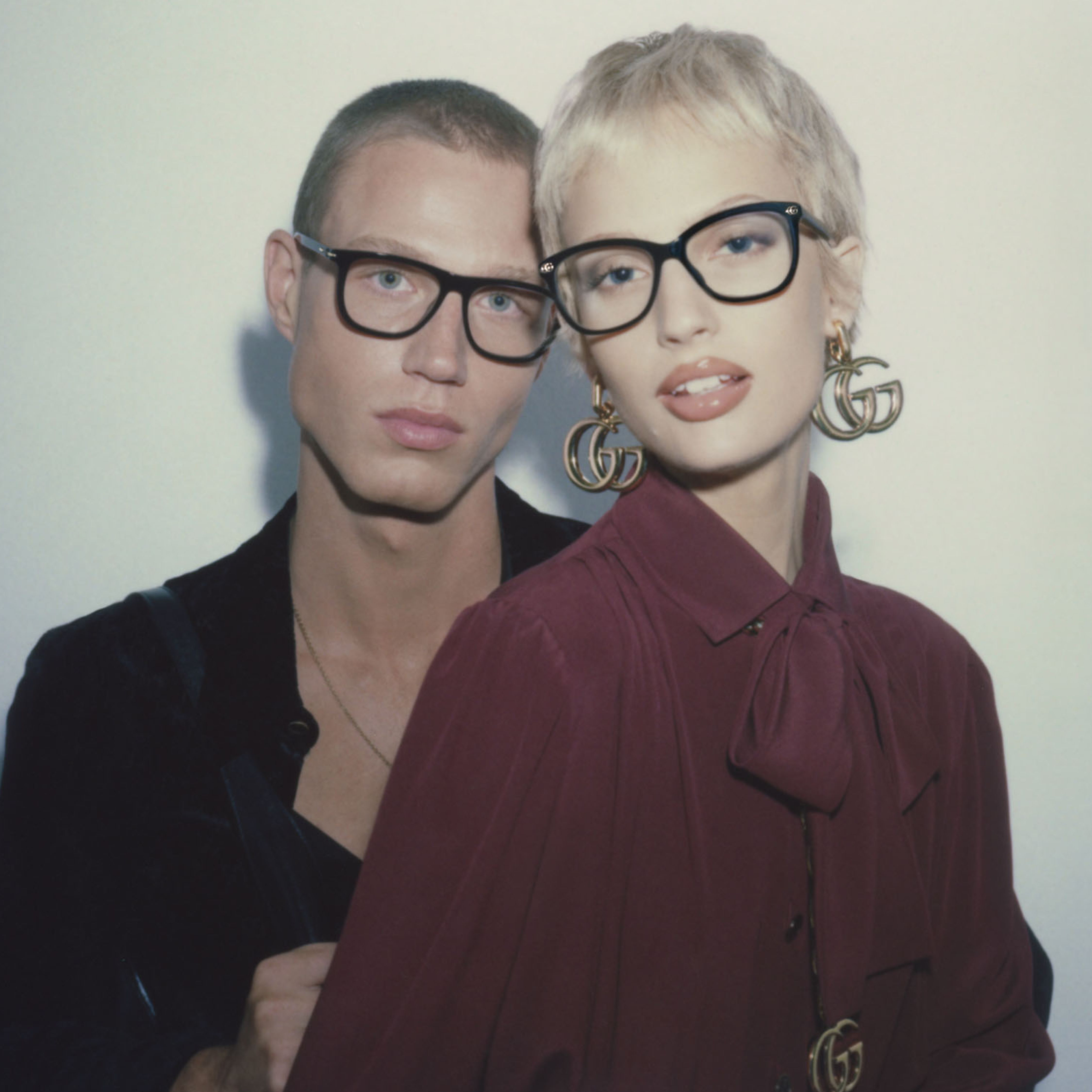 Two stylish individuals wearing glasses, posing closely together.