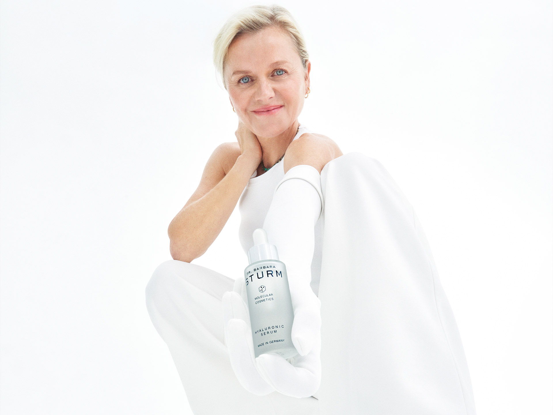 A woman in white clothing smiling and holding a water bottle.