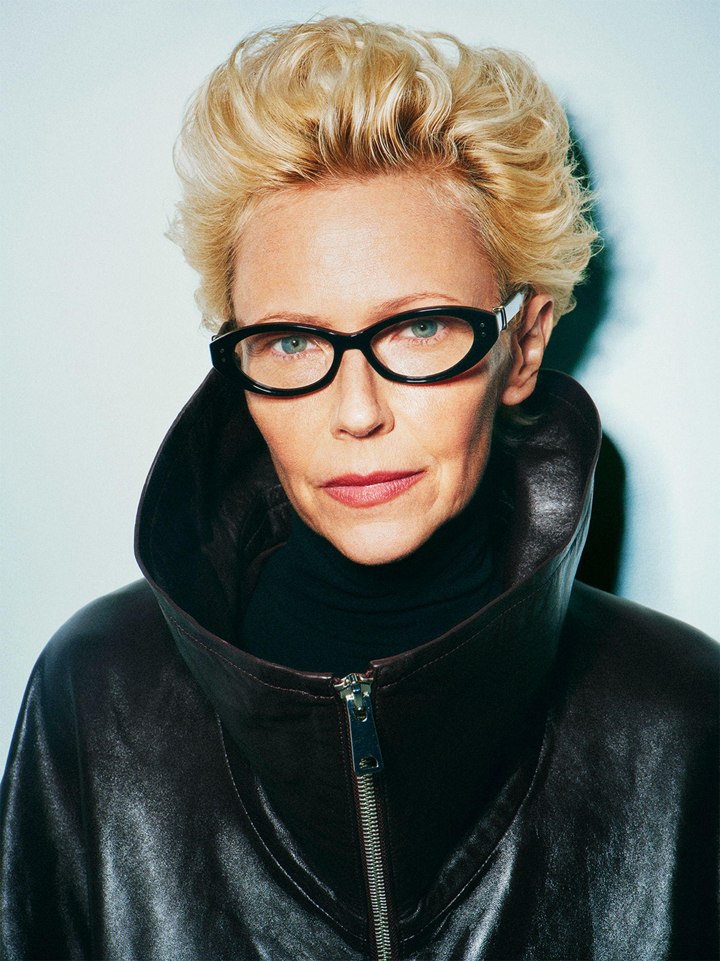 Portrait of a woman with short blonde hair wearing Robert Marc glasses and a stylish coat.