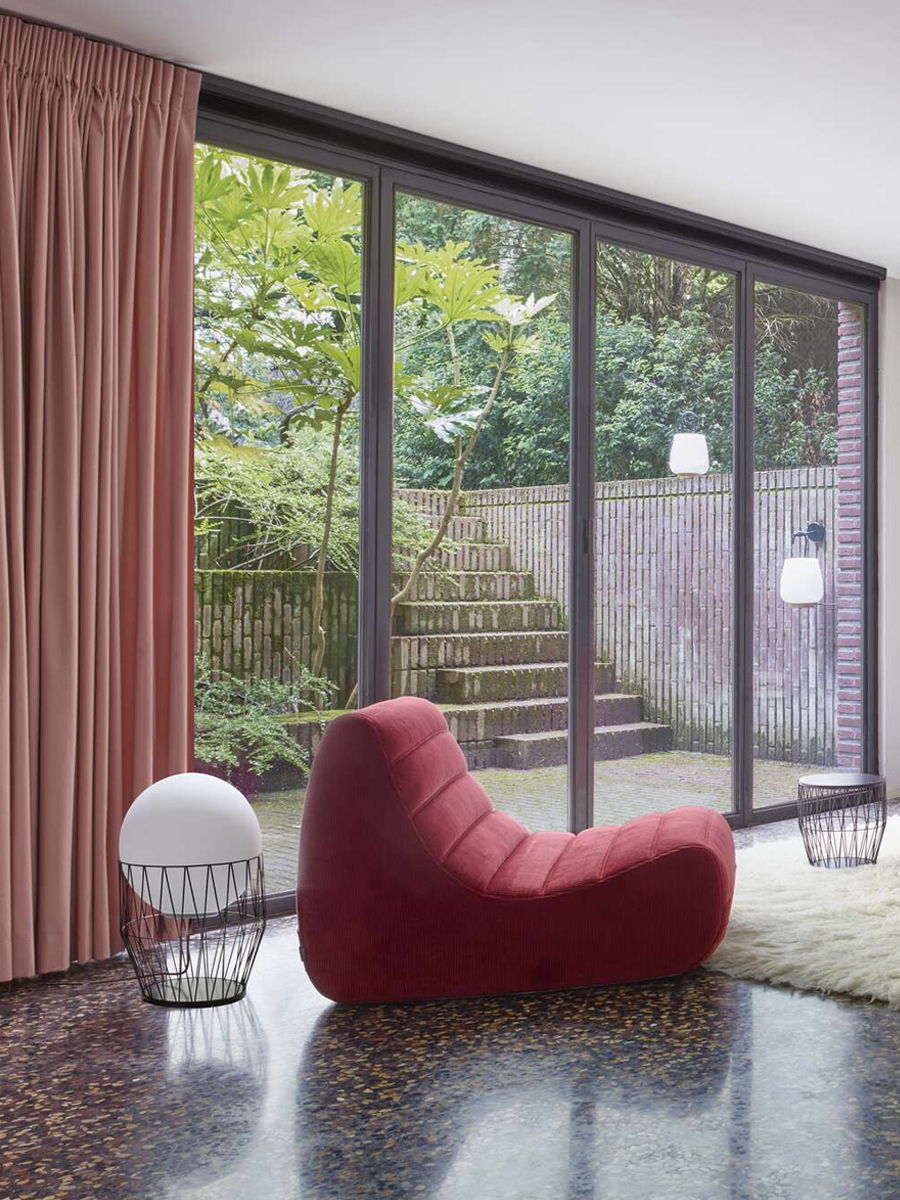 Interior with a red chair, curtains, and a view of a garden.