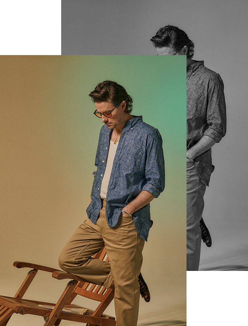 A man in a denim shirt stands beside a chair, looking down.
