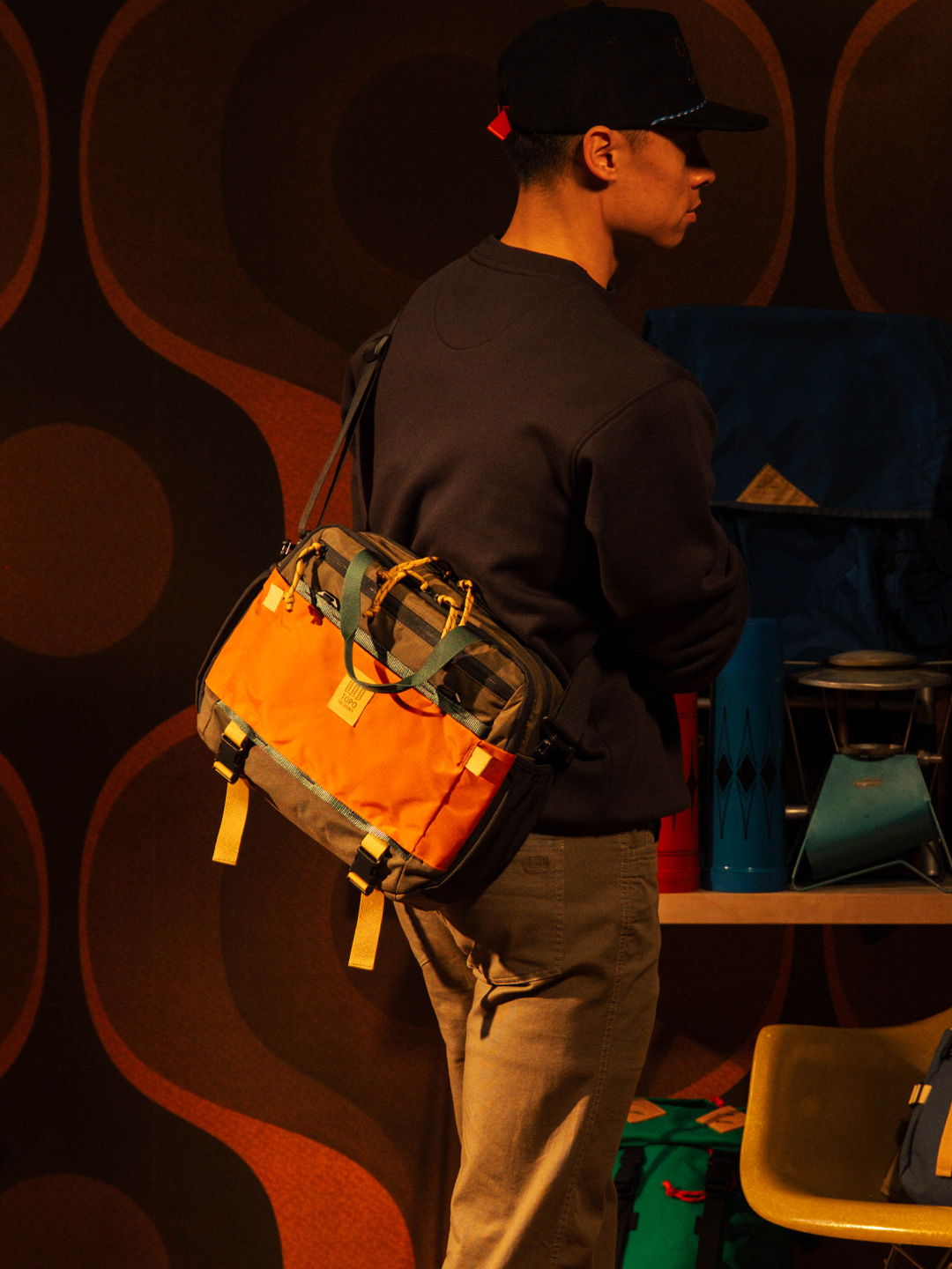 Person wearing a cap and carrying an orange bag in a stylish setting.