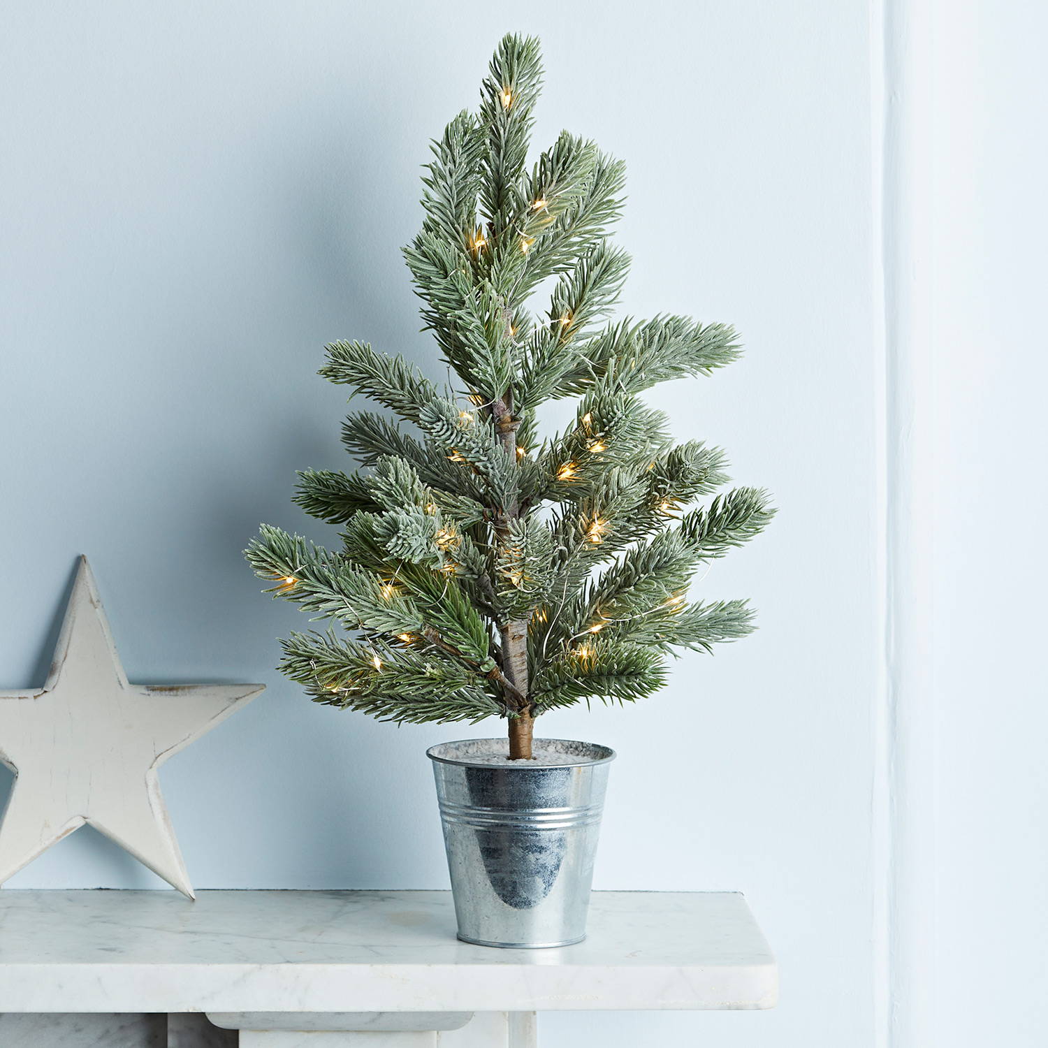 Mini potted Christmas tree entwined with micro lights sat on mantel