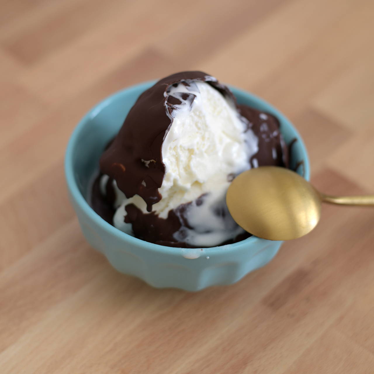Scoop of ice cream with a chocolate shell in a blue bowl.