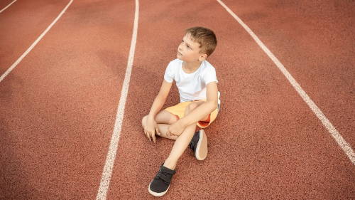 En ung gutt sitter midt i en løpebane – fysisk aktivitet kan utløse astma, så kanskje han måtte ta en pause eller ikke kan delta. 
