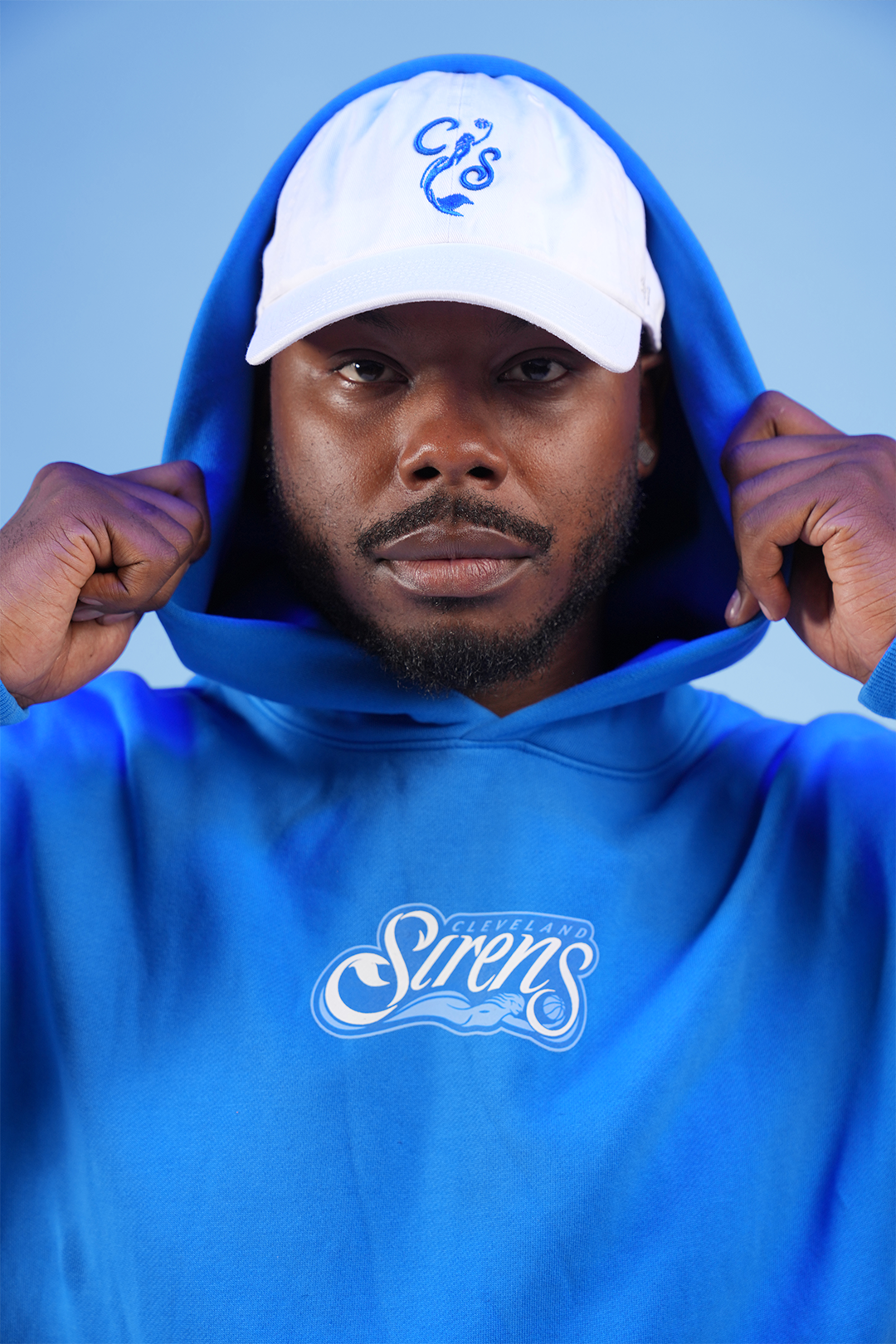 Man in blue hoodie and white cap against a blue background.
