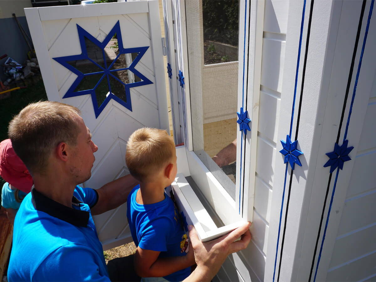  Father and son put a white flower box on the Kids Outdoor Playhouse Cornflower by WholeWoodPlayhouses