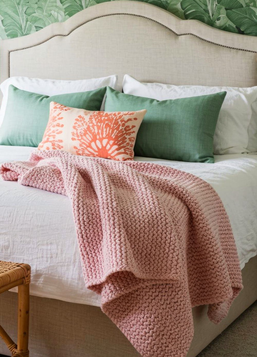 Cozy bed with pink blanket, green pillows, and decorative coral pillow.
