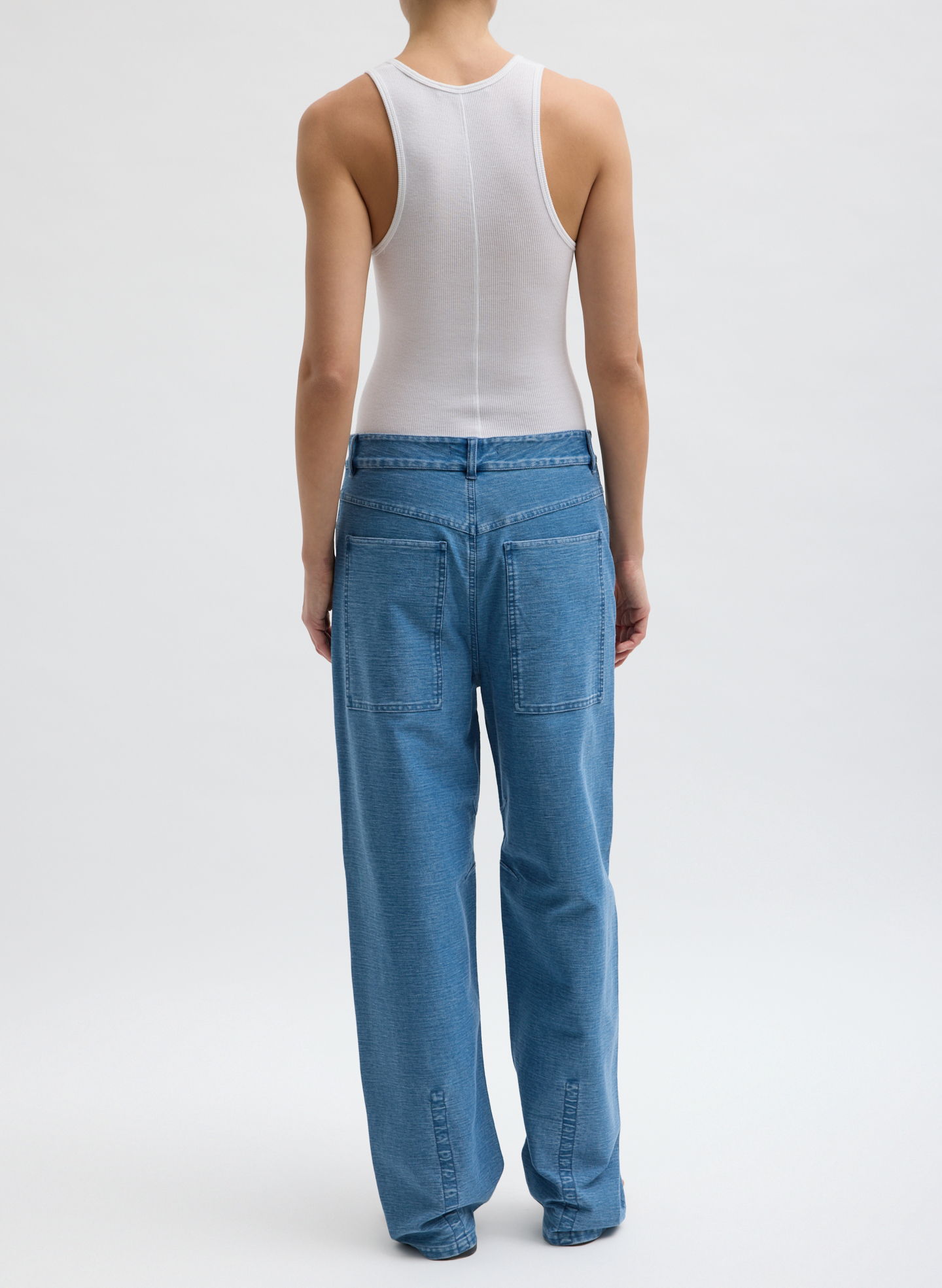 Person wearing a white tank top and blue jeans, viewed from behind.