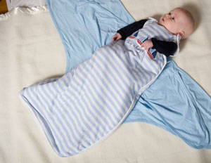 Baby lying in a sleeping bag ontop of a miracle blanket swaddle