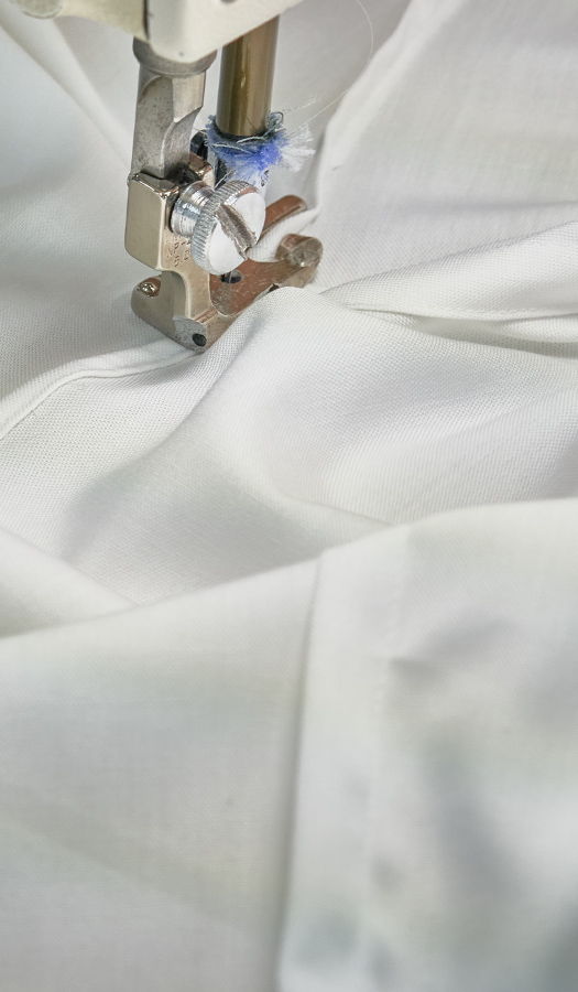 Close-up of a sewing machine stitching white fabric.