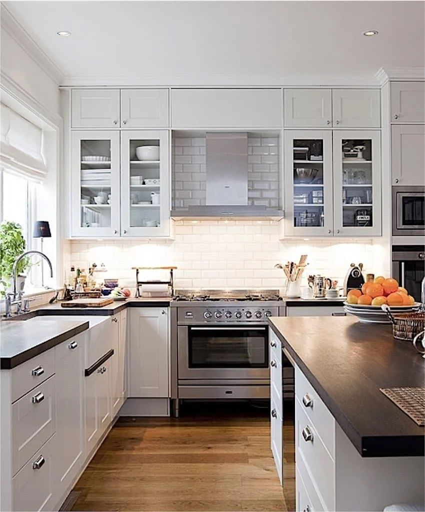 Modern kitchen with white cabinets, stainless steel appliances, and wooden floors.
