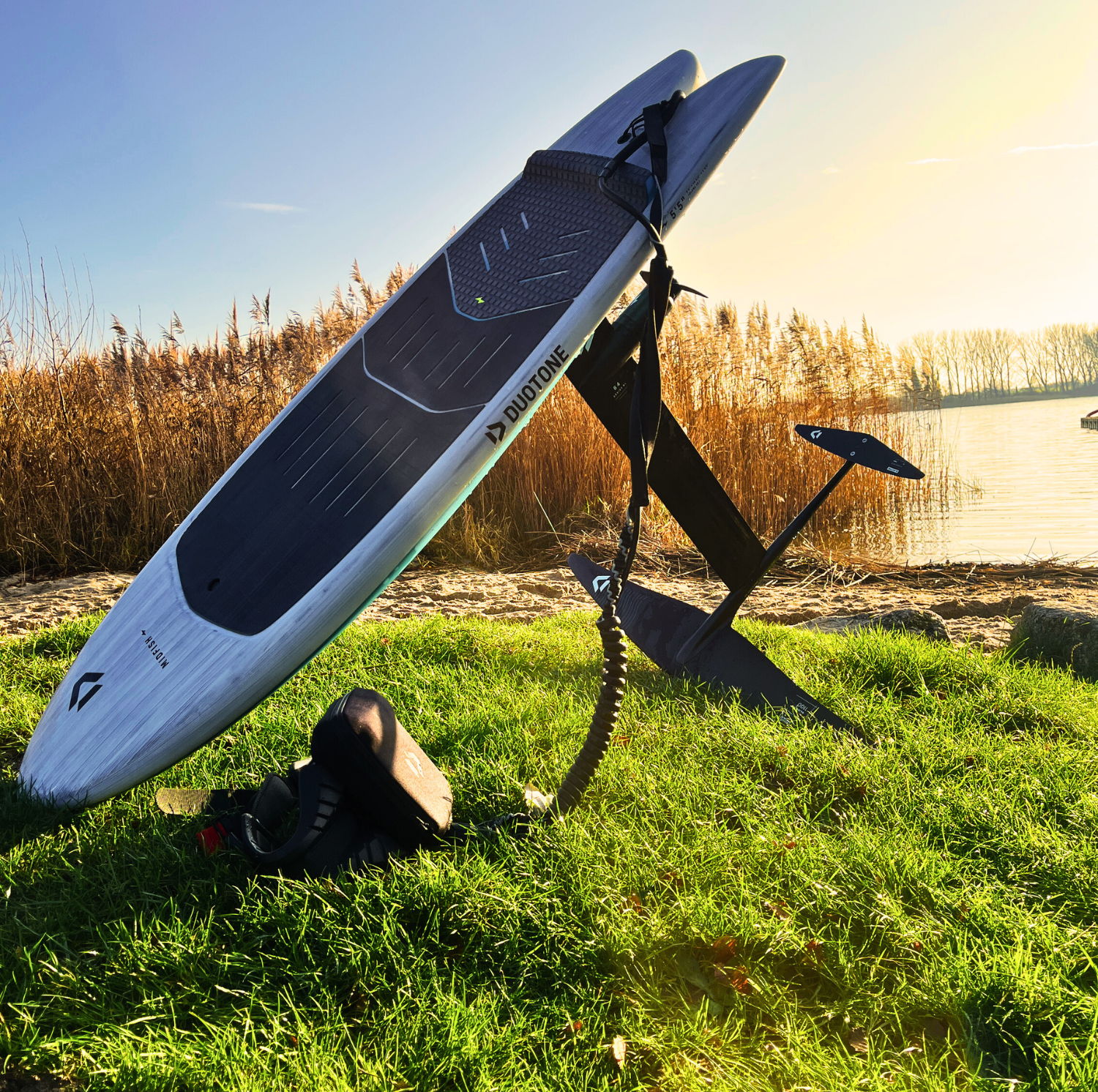 A surfboard with a e-foil on the grass near water.