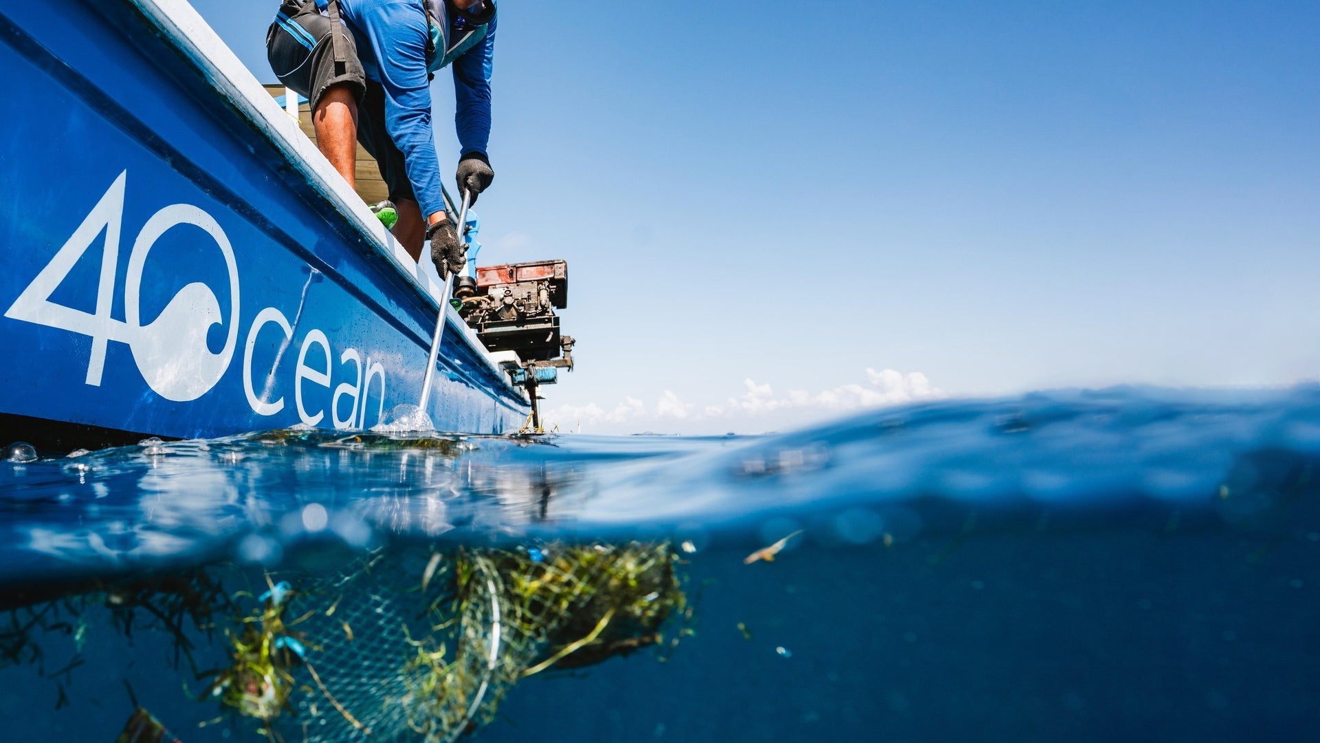 4ocean crew collecting plastic from the ocean beside a blue boat, photographed half above and half below the waterline.