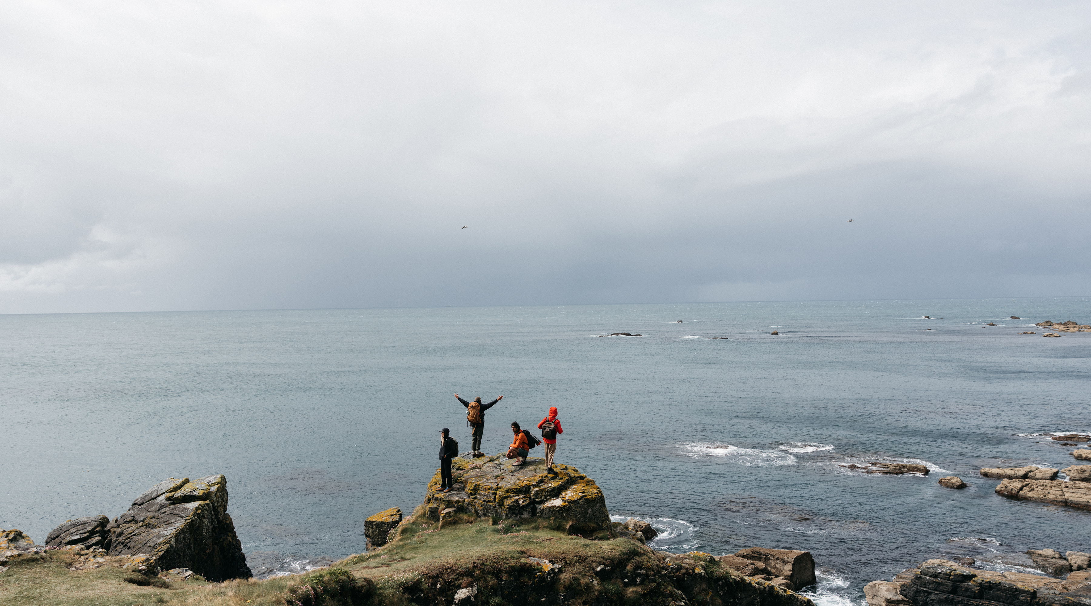 People celebrating on a rocky shore with a cloudy sky overhead.