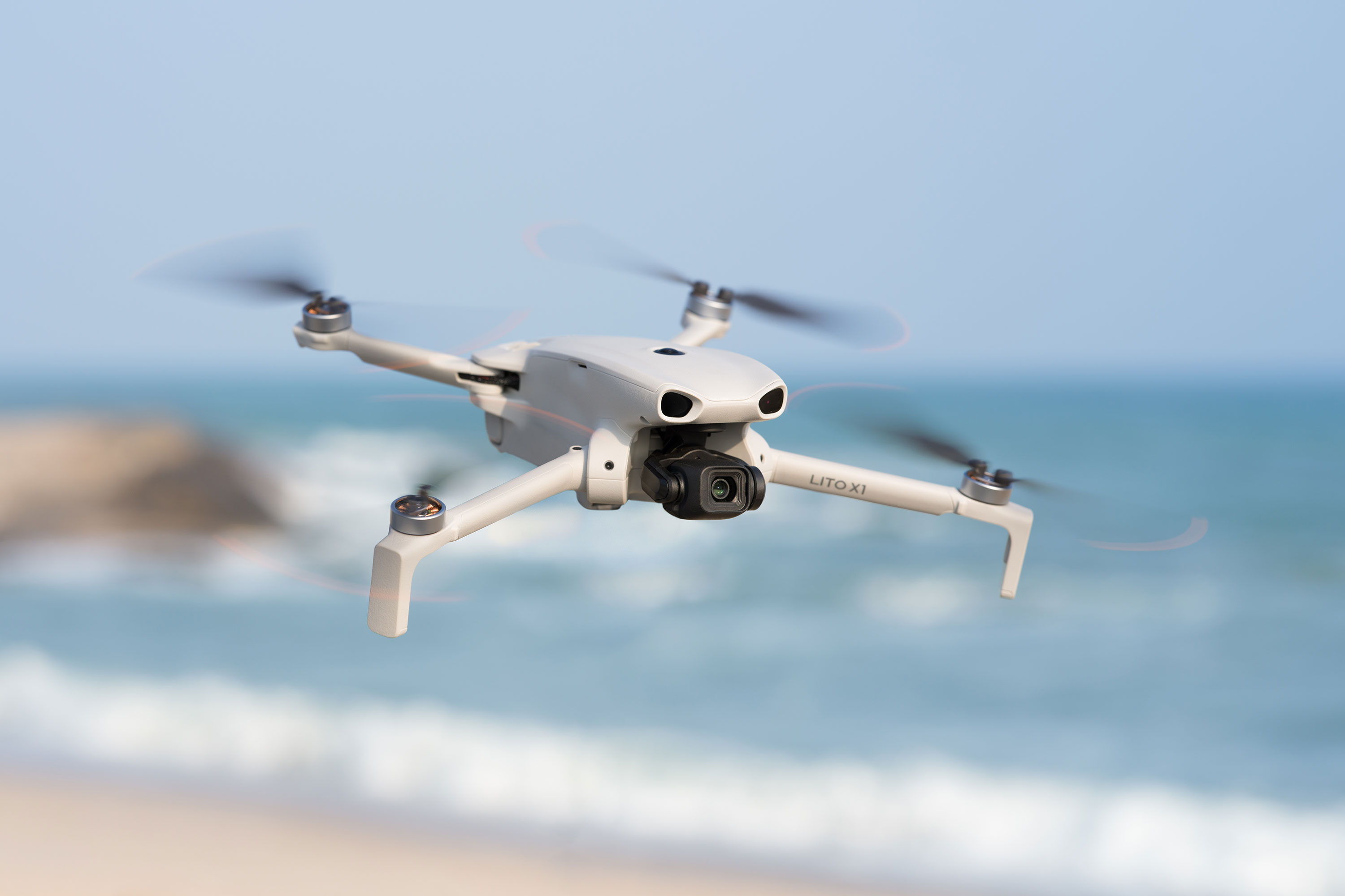 The DJI Lito X1 flying above a beach with ocean waves in the background.