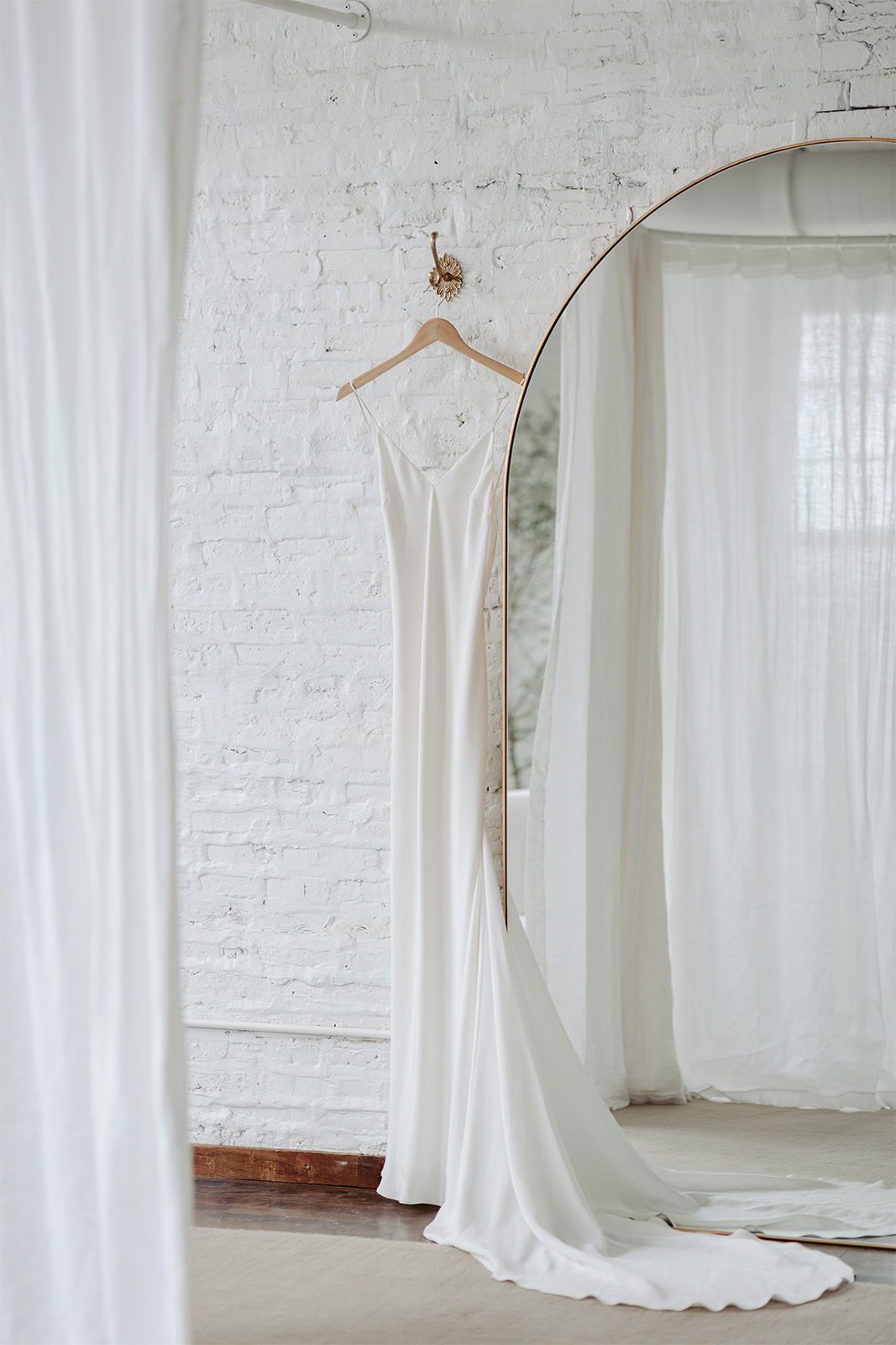 A white dress hanging in a bright, minimalist room with a mirror.