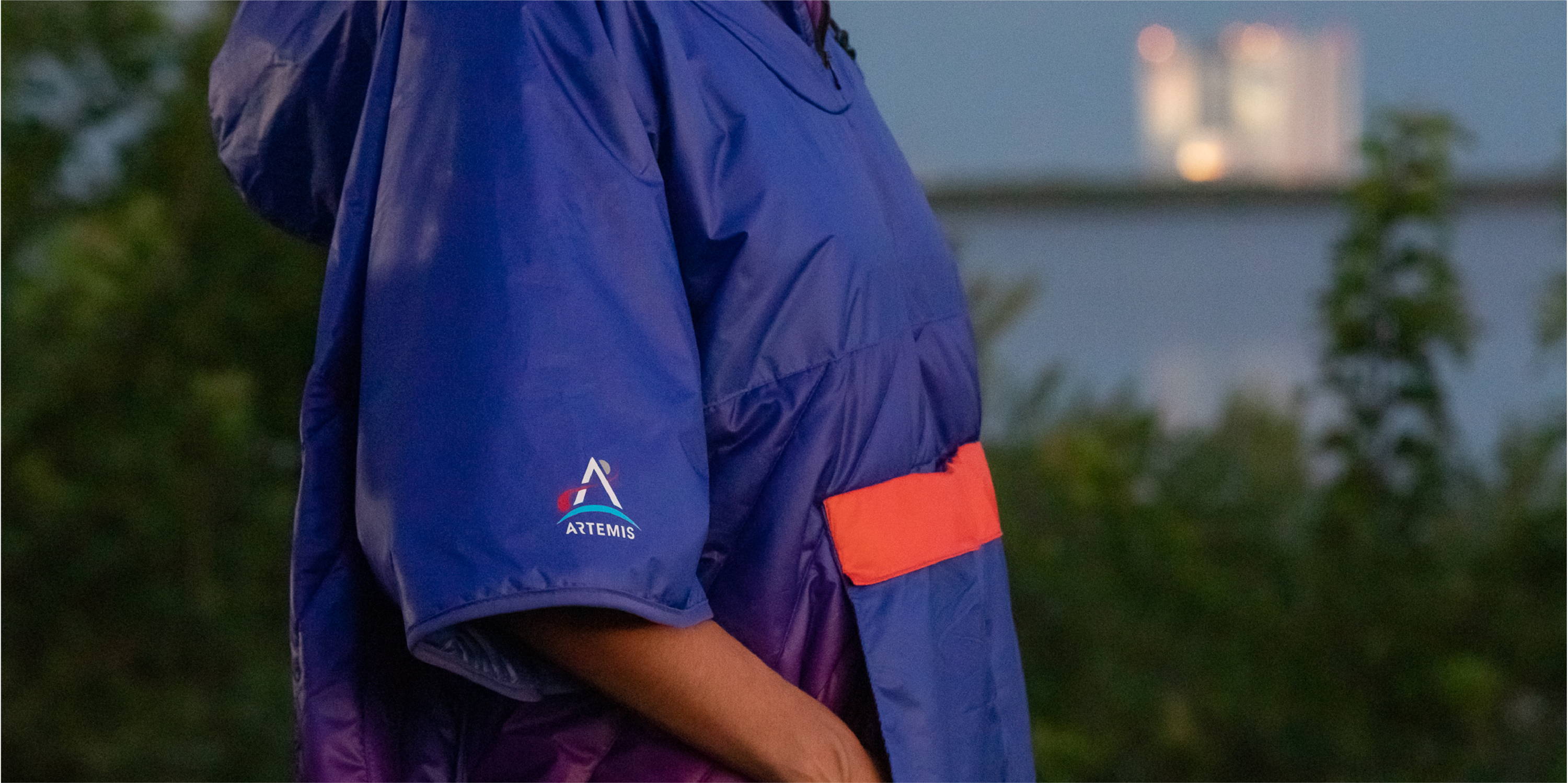 Woman wearing Rumpl ARTEMIS nasa poncho near rocket takeoff