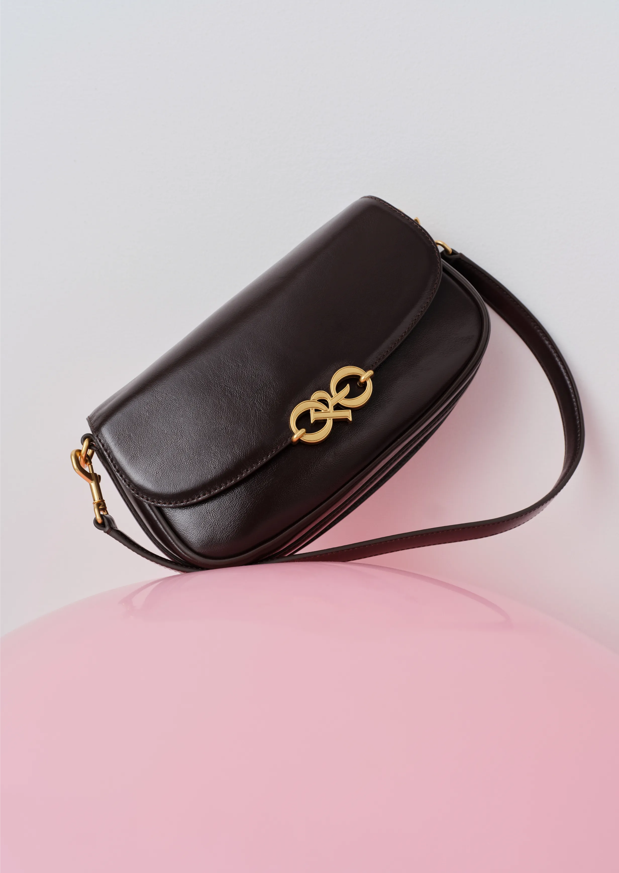 Black leather handbag with gold emblem on a pink surface.