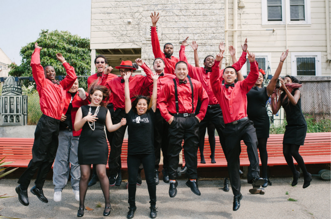 Group of people in red and black outfits jumping joyfully outdoors.
