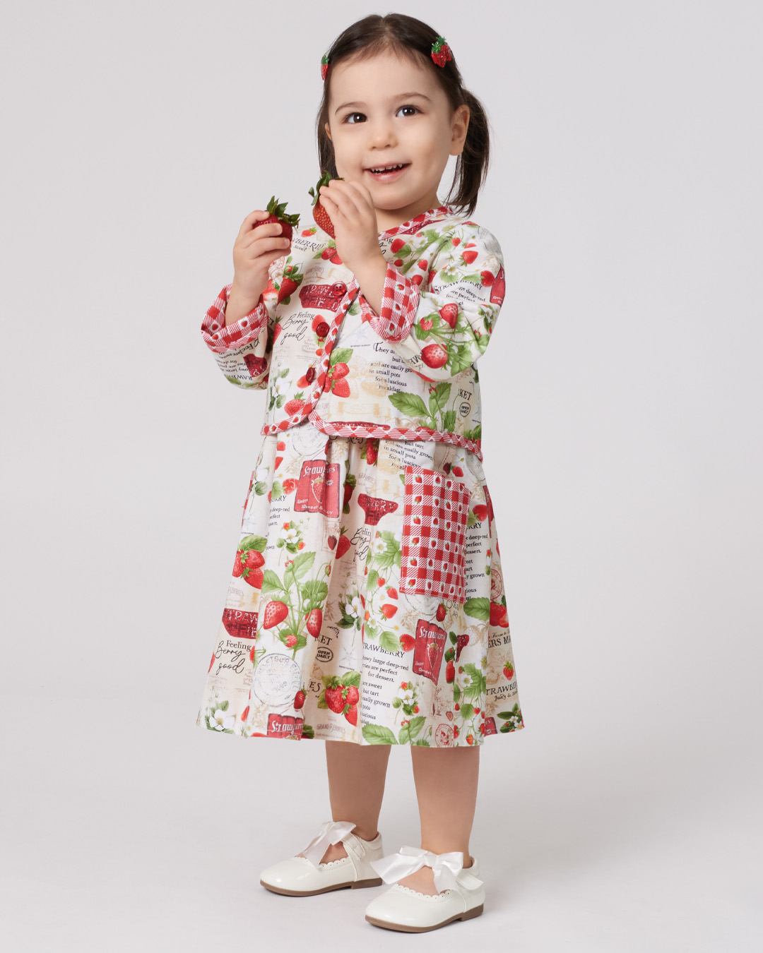 A young girl in a colorful dress, holding a small object and smiling.