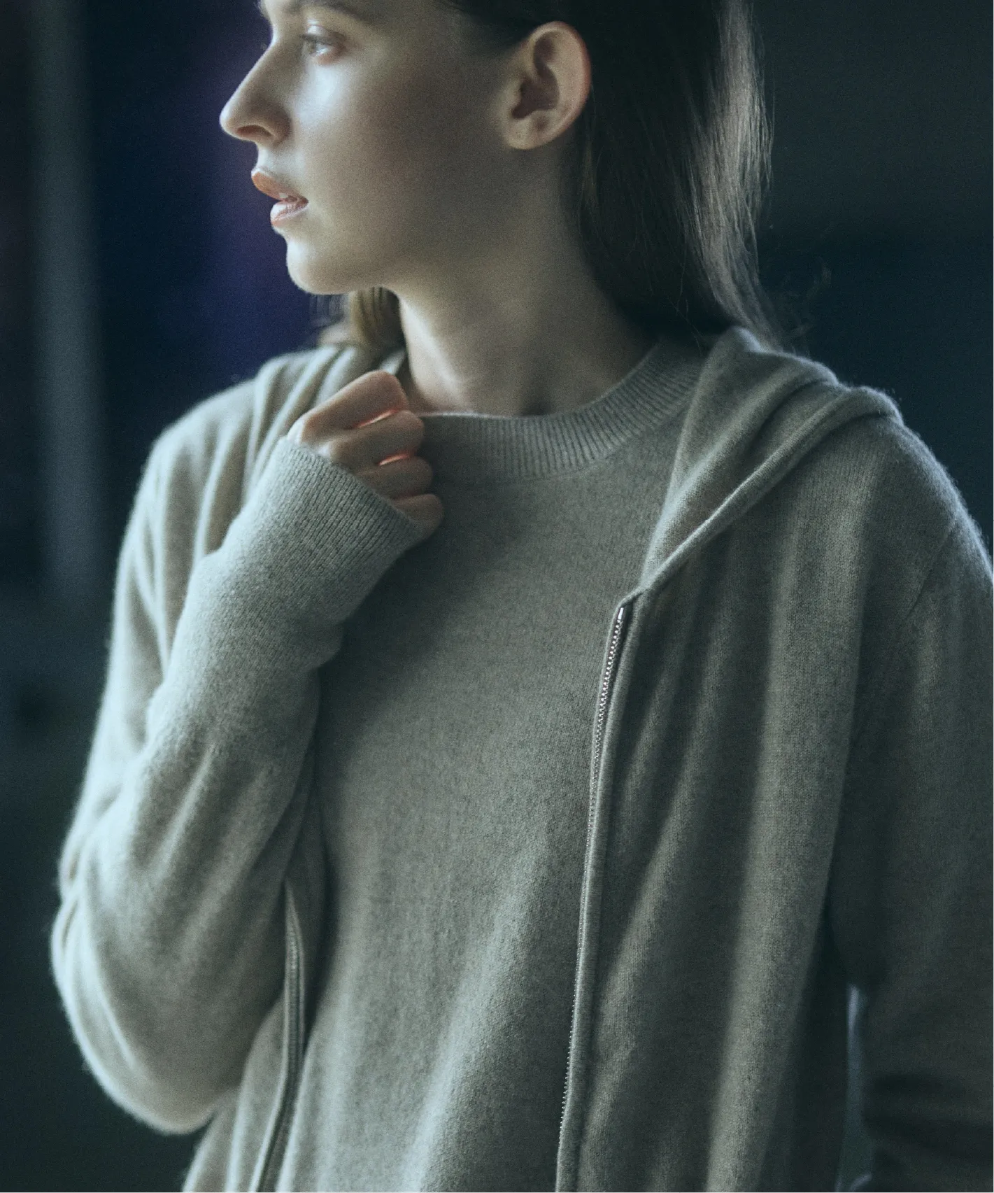 A young woman in a gray hoodie, looking thoughtfully to the side.