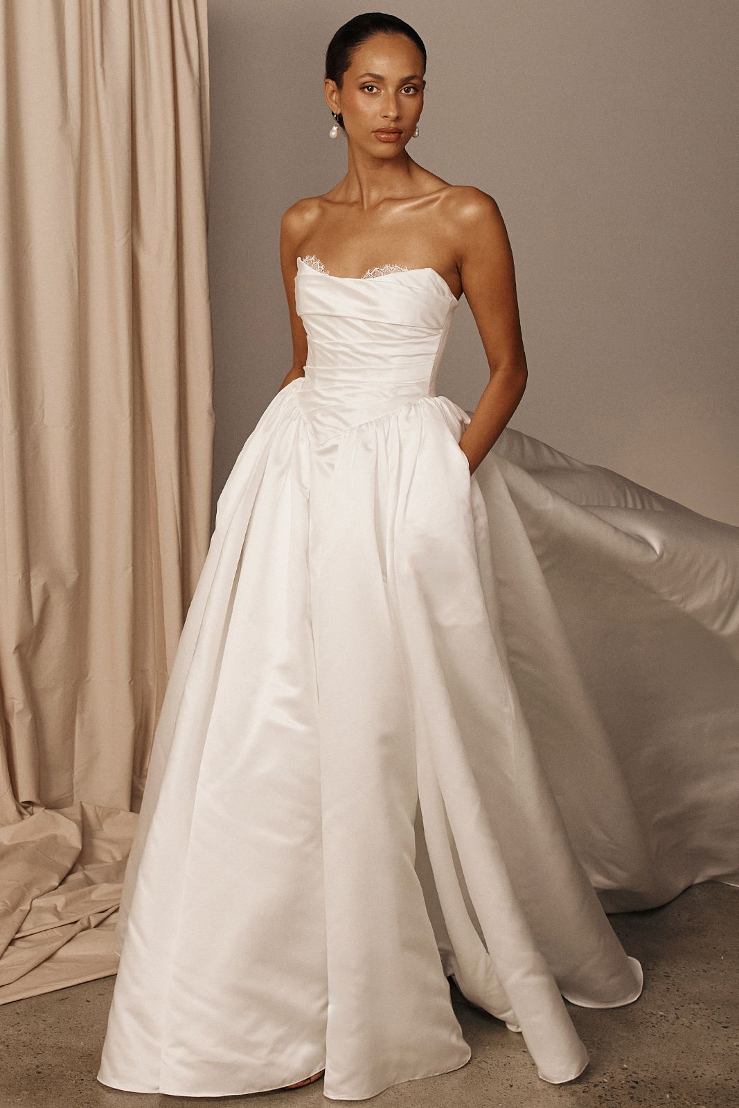 Model in a strapless white gown with pockets, standing against a neutral background.