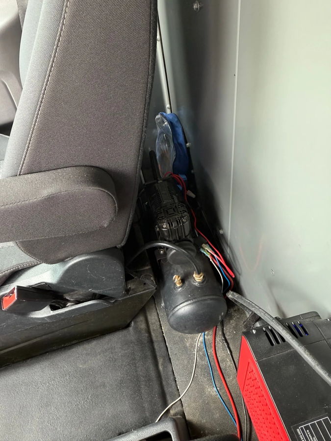 Black air compressor tank red power inverter wiring behind gray seat cargo area Taylor's Ford Transit 228H gallery photo 5
