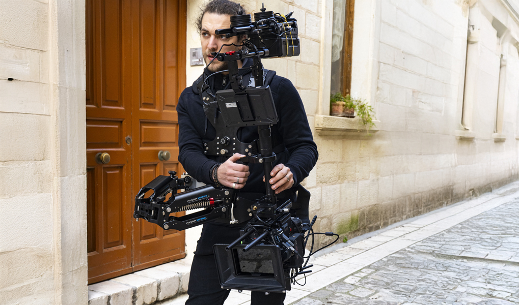 Person carrying a large camera rig on a street.
