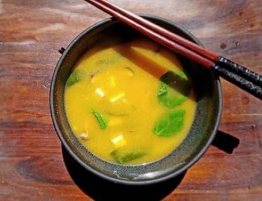 Bowl of soup with green vegetables and chopsticks on a wooden table.