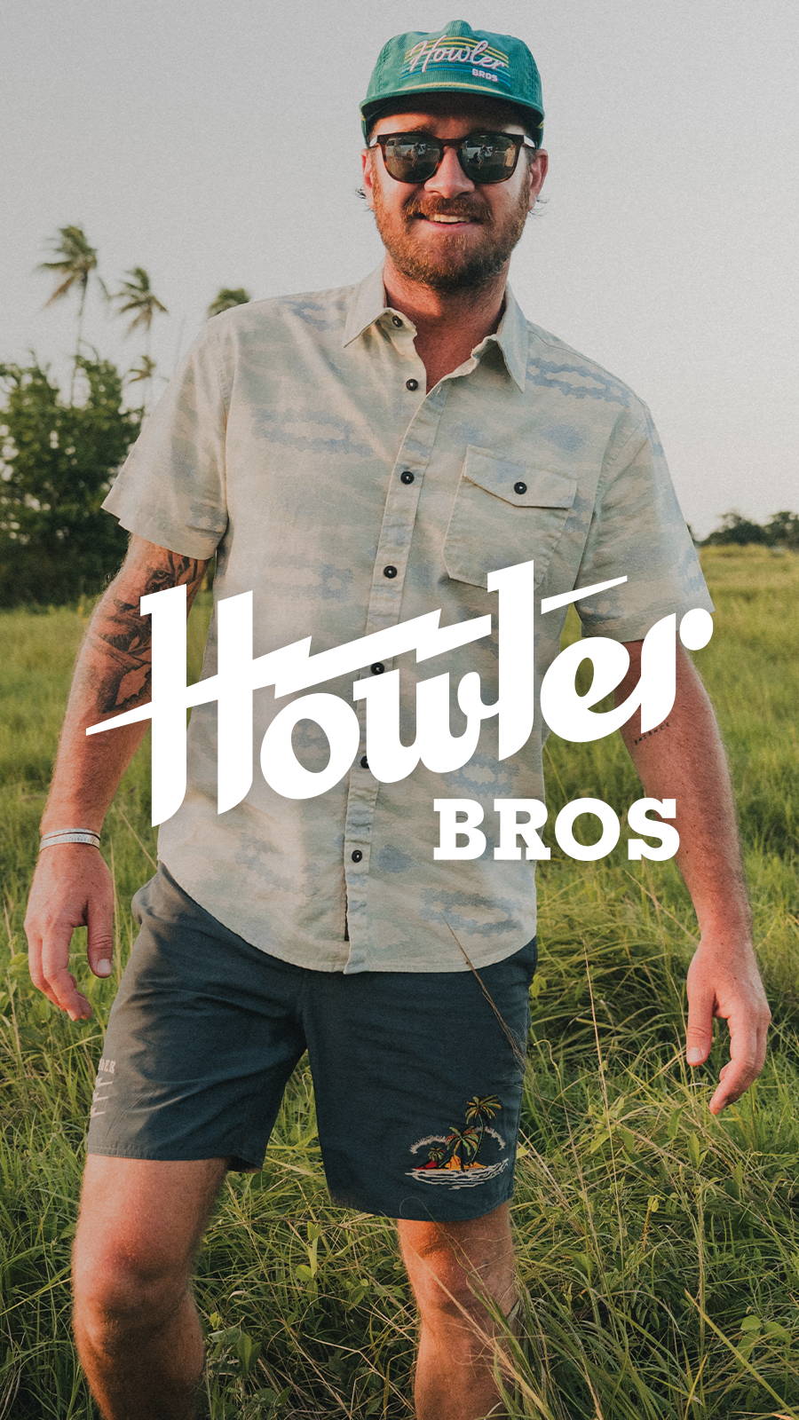 Man Bettering in field wearing Howler Bros button up, shorts, hat and sunglasses