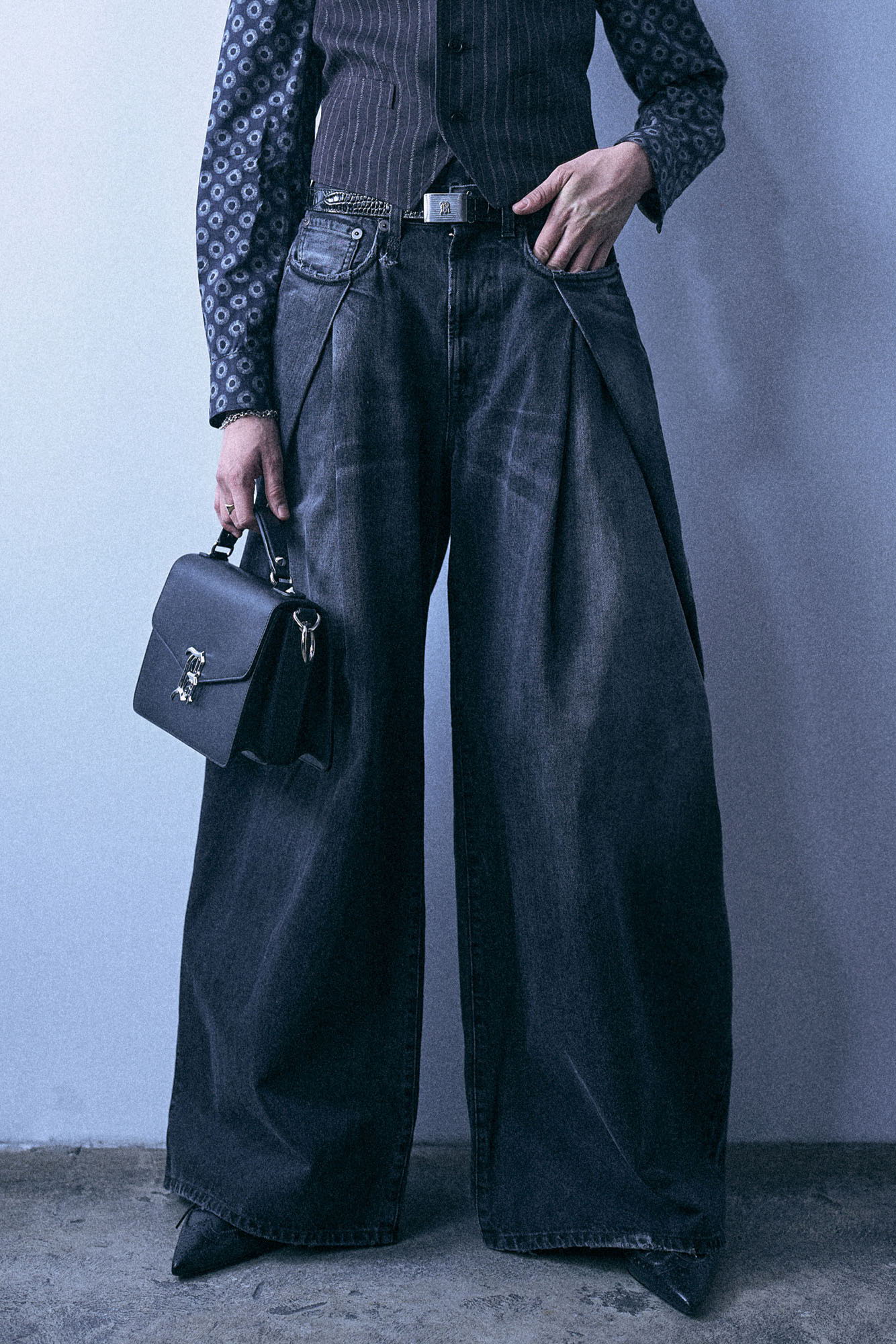 Person wearing oversized denim pants and holding a small handbag.